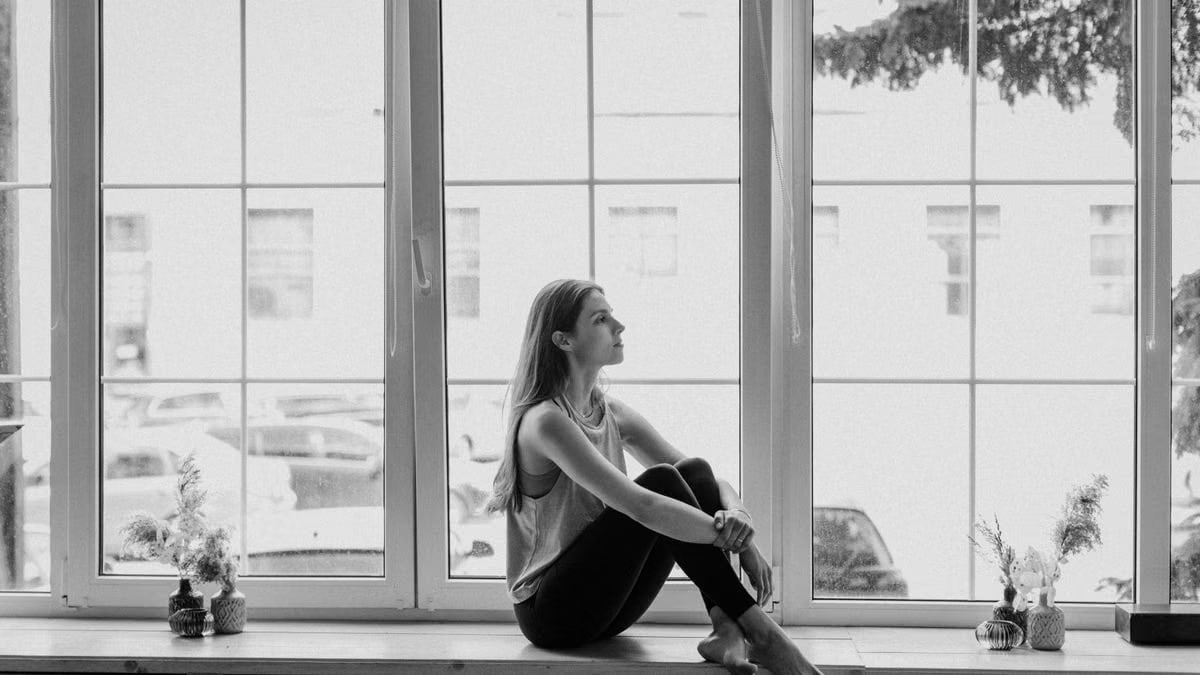 Black and white photo of a young woman sitting on a windowsill and deep in thought.